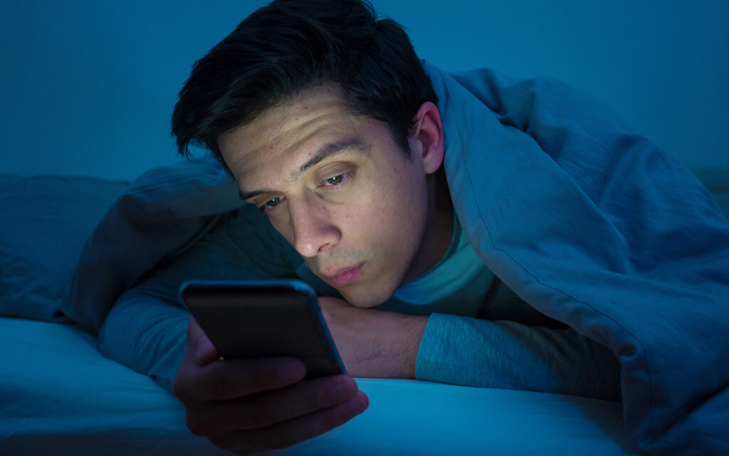 young man using his phone at night in bed